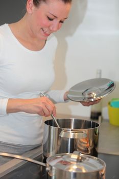 Smiling housewife cooking in the kitchen stirring the contents of a pot on the stove