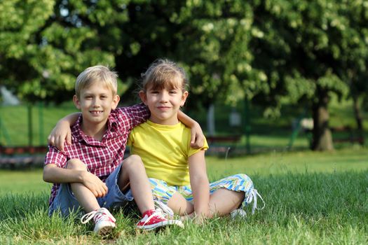 happy little girl and boy sitting on grass