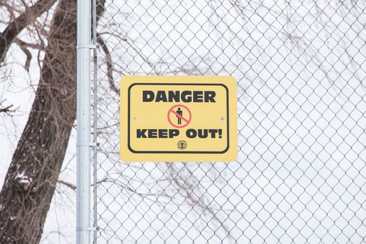 Danger keep out sign on metal fence in winter.