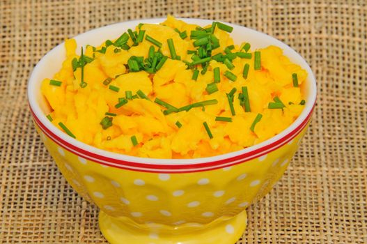Scrambled eggs with chives in a yellow bowl on beige napkins