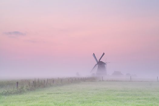 windmill on meadow in morning fog at sunrise