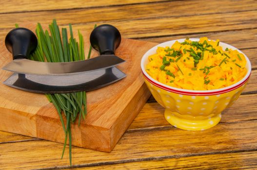 Scrambled eggs with chives in a yellow bowl and a herb chopper on a wooden table