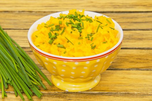 Scrambled eggs with chives in a yellow bowl on a wooden table