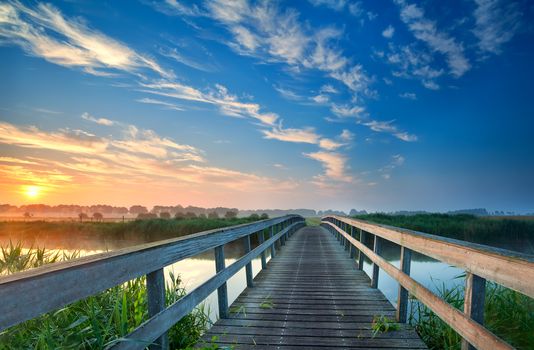 charming wooden bridge for bicycles over river at sunrise