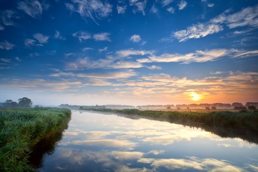 orange sunrise over wide river with reflected blue sky