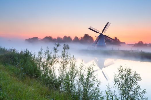 charming Dutch windmill by river at sunrise