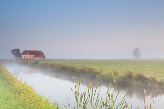 farmhouse on riverside in morning fog during sunrise