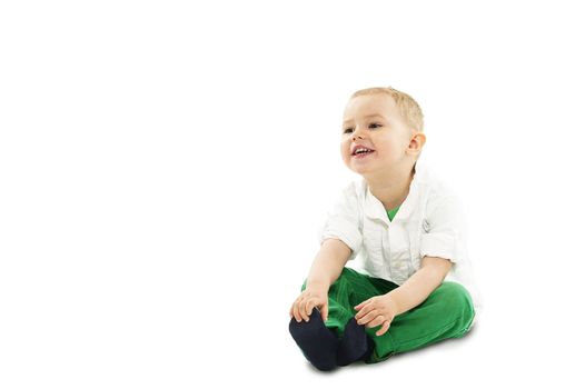 Adorable handsome young boy sitting on the floor bending forwards laughing and holding his toe isolated on white with copyspace