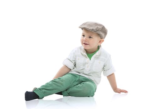 Handsome little boy in a cloth cap and smart green outfit sitting relaxing on a white studio floor with copy space