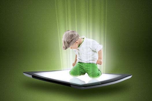 Conceptual image of a cute dapper little boy in a cap kneeling on the touch screen of a modern tablet computer with data and information streaming around him forming a beam