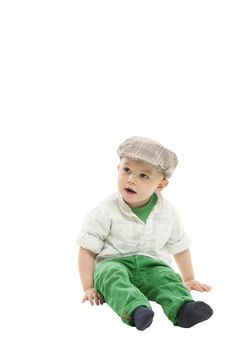 Sweet little boy wearing a cloth cap sitting on the floor with his legs outstretched looking to the left of the frame isolated on white with copyspace