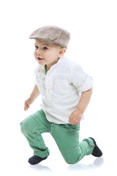 Dapper little boy in a cute outfit with a cloth cap, white shirt and green trousers rising to his feet with a look of delighted anticipation, isolated on white with a small reflection
