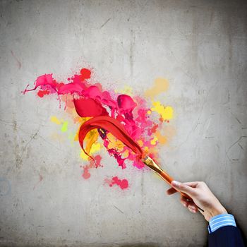 Close-up of human hand holding paint brush making colorful paint splashes