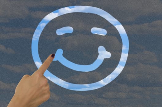 hand drawing a smiley face on a dirty window with a finger revealing clear blue sky on the other side