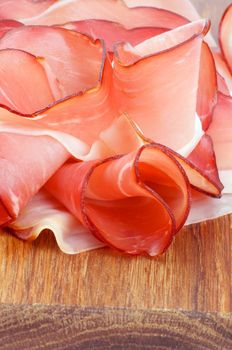 Arrangement of Delicious Prosciutto Slices on Edge of Wooden Cutting Board closeup