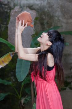 Asian girl by foliage drinking from clay pot