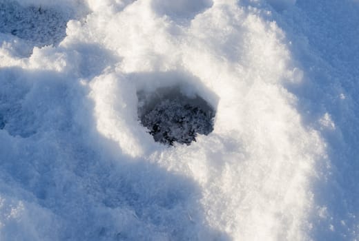 Closeup of frozen fishing ice hole on winter lake in evening sunlight shadows.