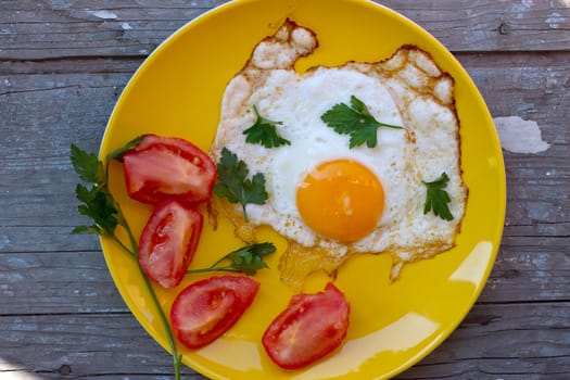 Scrambled eggs with tomato in a yellow plate on the old board