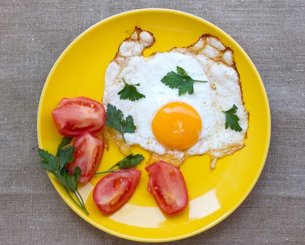 scrambled eggs with tomato in a yellow plate on a burlap tablecloth