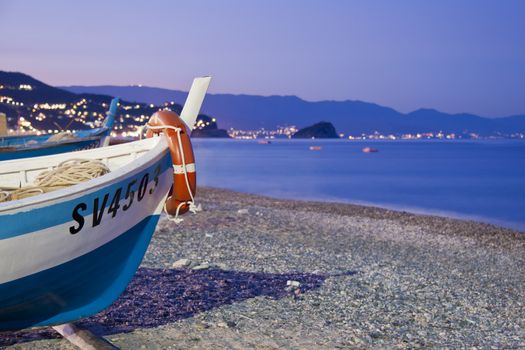 Boat on the cobblestones beach of Noli, facing the mediterranean sea and the gulf of Noli, during the sunset