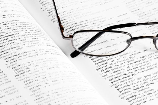 opened russian-serbian dictionary book with eye glasses