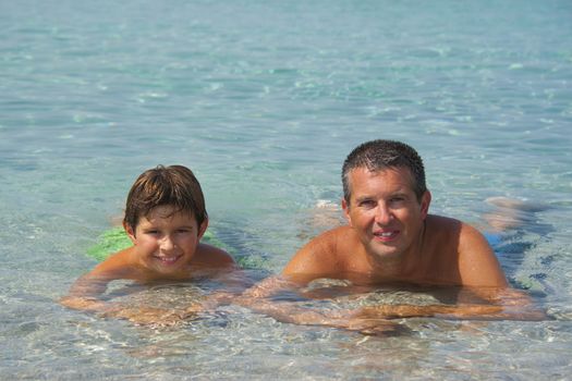 Father and son liying in the sea in Sardinia