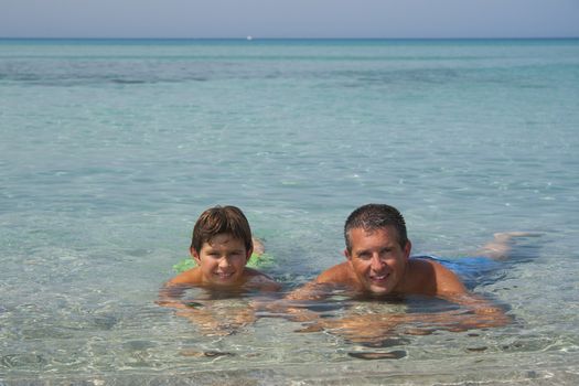 Father and son liying in the sea in Sardinia