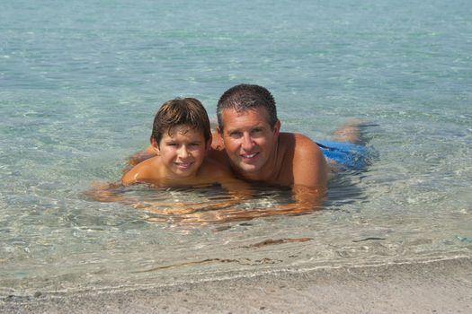 Father and son liying in the sea in Sardinia