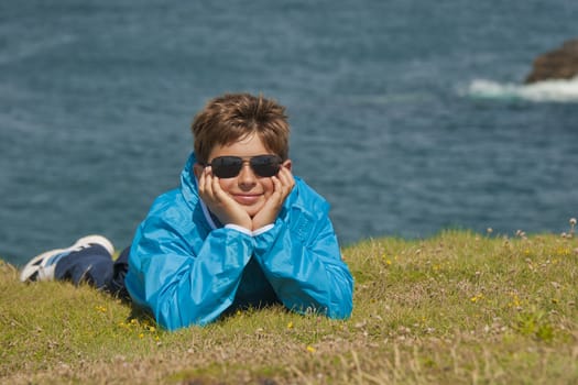 young boy laying down on the grass in front of the ocean