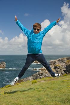 young boy jumping on the grass in front of the ocean during a beautiful sunny day