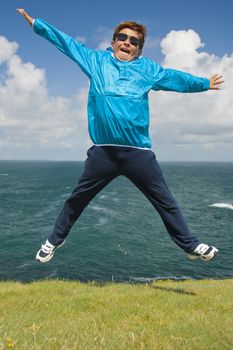 young boy jumping on the grass in front of the ocean during a beautiful sunny day