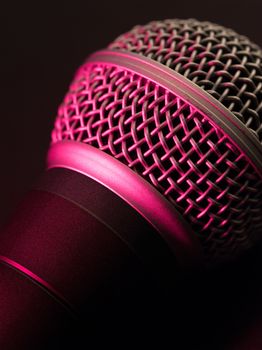 Macro photo of a vocal microphone lit with stage lights.