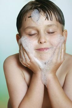 A young male child washes his face with bubbly soap and water