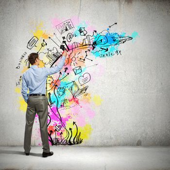 Back view of businessman drawing colorful business ideas on wall