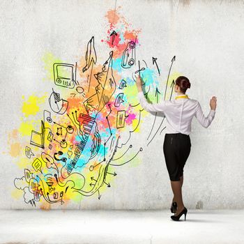 Back view of businesswoman drawing colorful business ideas on wall