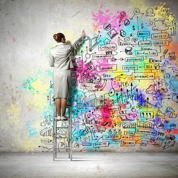 Back view of businesswoman drawing colorful business ideas on wall