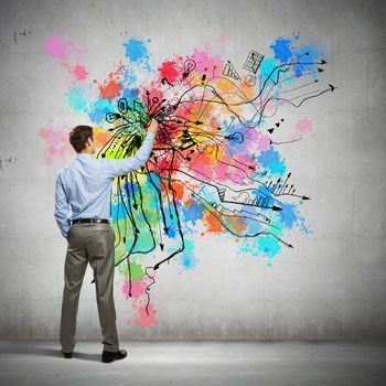 Back view of businessman drawing colorful business ideas on wall