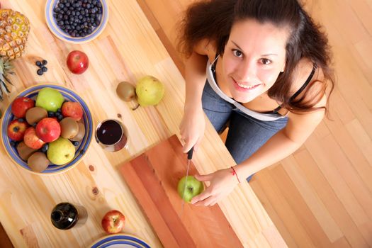 A young adult woman cutting fruits in the kitchen.