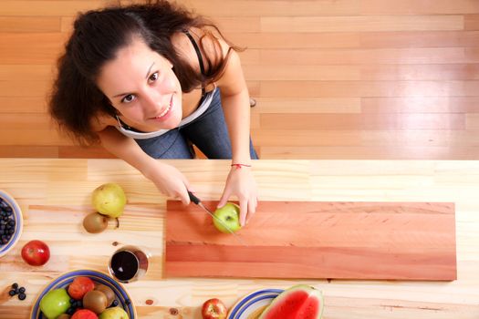 A young adult woman cutting fruits in the kitchen.