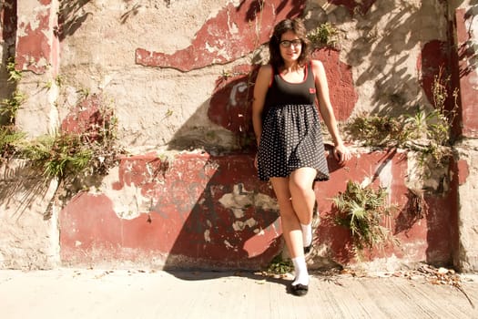 A vintage style dressed girl leaning at a graffiti wall and enjoying the sunlight.