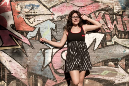 A vintage style dressed girl leaning at a graffiti wall and enjoying the sunlight.