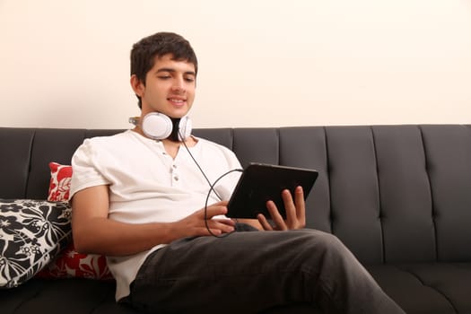 A young, latin man with a Tablet PC and Headphones on the Sofa
