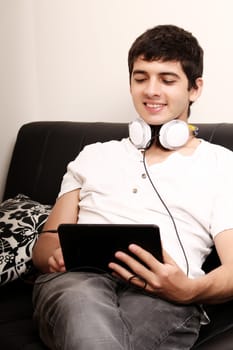 A young, latin man with a Tablet PC and Headphones on the Sofa
