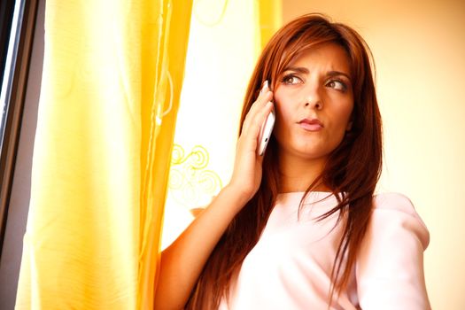 A beautiful woman waiting at the window while talking on the phone.