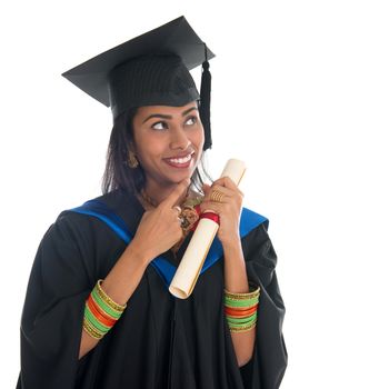 Happy Indian university student in graduation gown and cap holding diploma certificate thinking. Portrait of mixed race Asian Indian and African American female model standing isolated on white background.