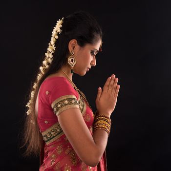 Portrait of beautiful young Indian woman prayer in traditional sari dress, isolated on black background.