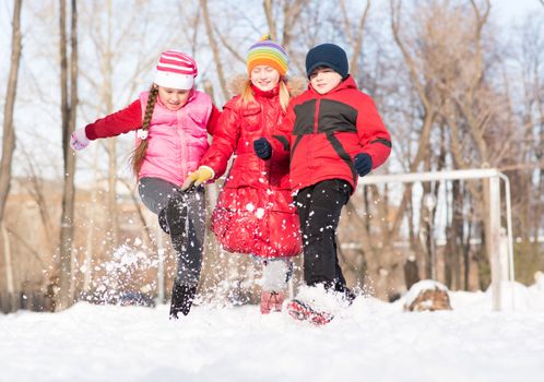 Boy and girls playing with snow in winter park, spending time together outdoors