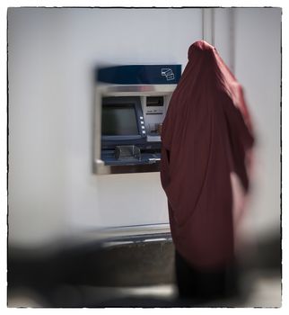 Unidentified muslim woman seen from behind by cashpoint drawing cash.