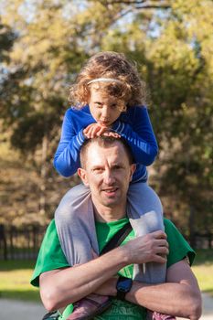 Father giving daughter piggyback ride in a park during sunny day.
