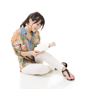 Young asian woman sitting on the ground and reading a book. Portrait isolated on white background.